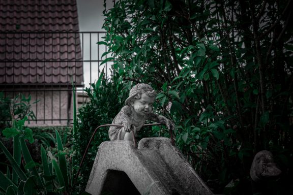 Ein Kind, das sich bereit macht zu rutschen – eingefroren als Gartenfigur. Trotzdem sieht und spürt man die Freude des Kindes.