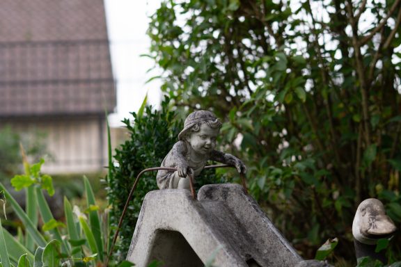 Ein Kind, das sich bereit macht zu rutschen – eingefroren als Gartenfigur. Trotzdem sieht und spürt man die Freude des Kindes.
