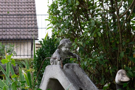 Ein Kind, das sich bereit macht zu rutschen – eingefroren als Gartenfigur. Trotzdem sieht und spürt man die Freude des Kindes.