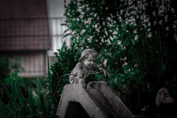 Ein Kind, das sich bereit macht zu rutschen – eingefroren als Gartenfigur. Trotzdem sieht und spürt man die Freude des Kindes.