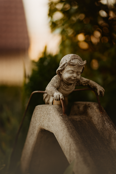 Ein Kind, das sich bereit macht zu rutschen – eingefroren als Gartenfigur. Trotzdem sieht und spürt man die Freude des Kindes.